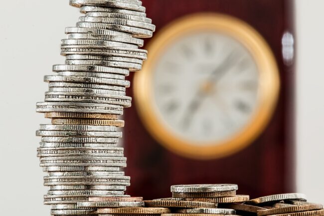 Pile de pièces de monnaie devant une horloge